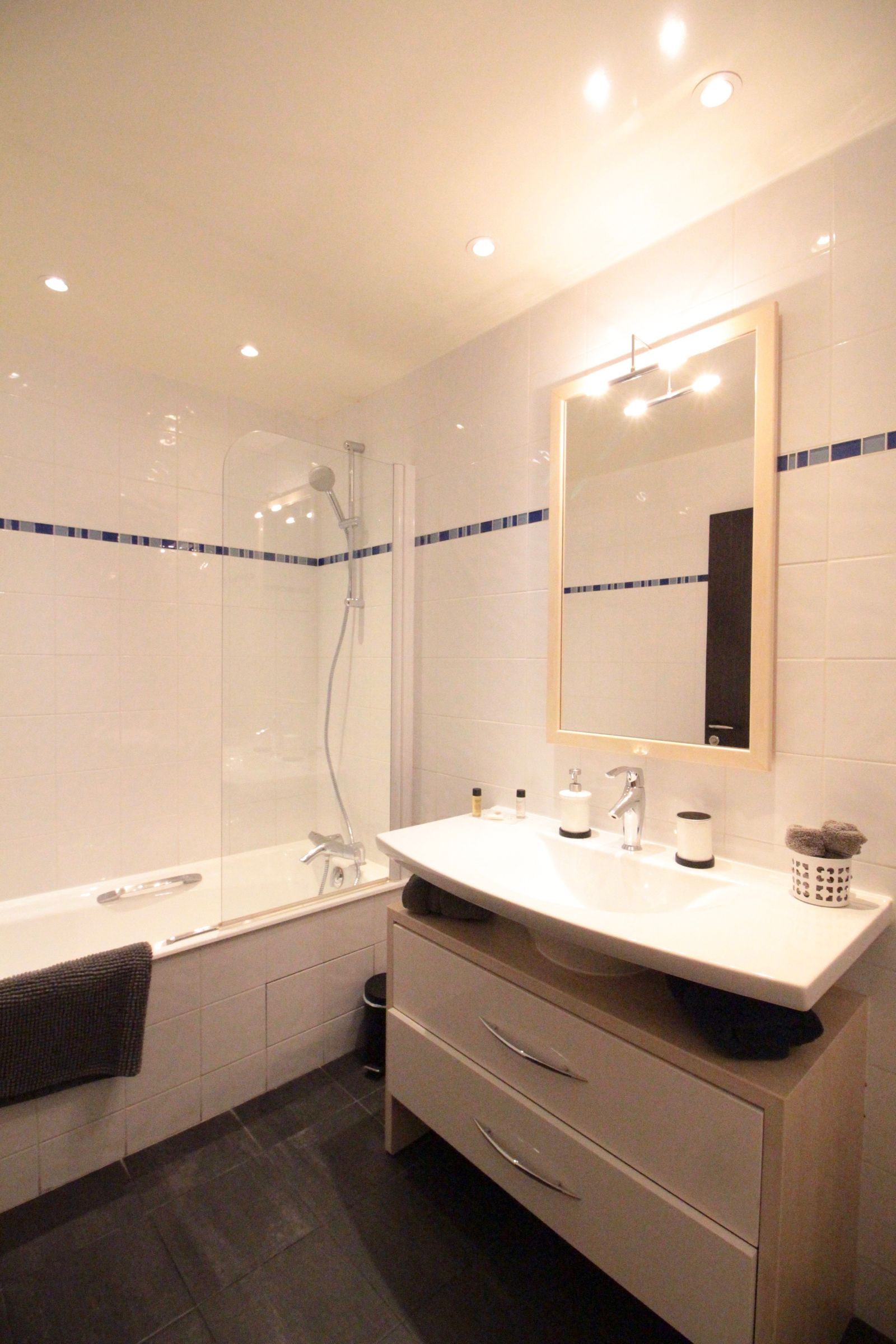 Spacious bathroom with bathtub, walk-in shower, wooden vanity, and blue mosaic tile accents