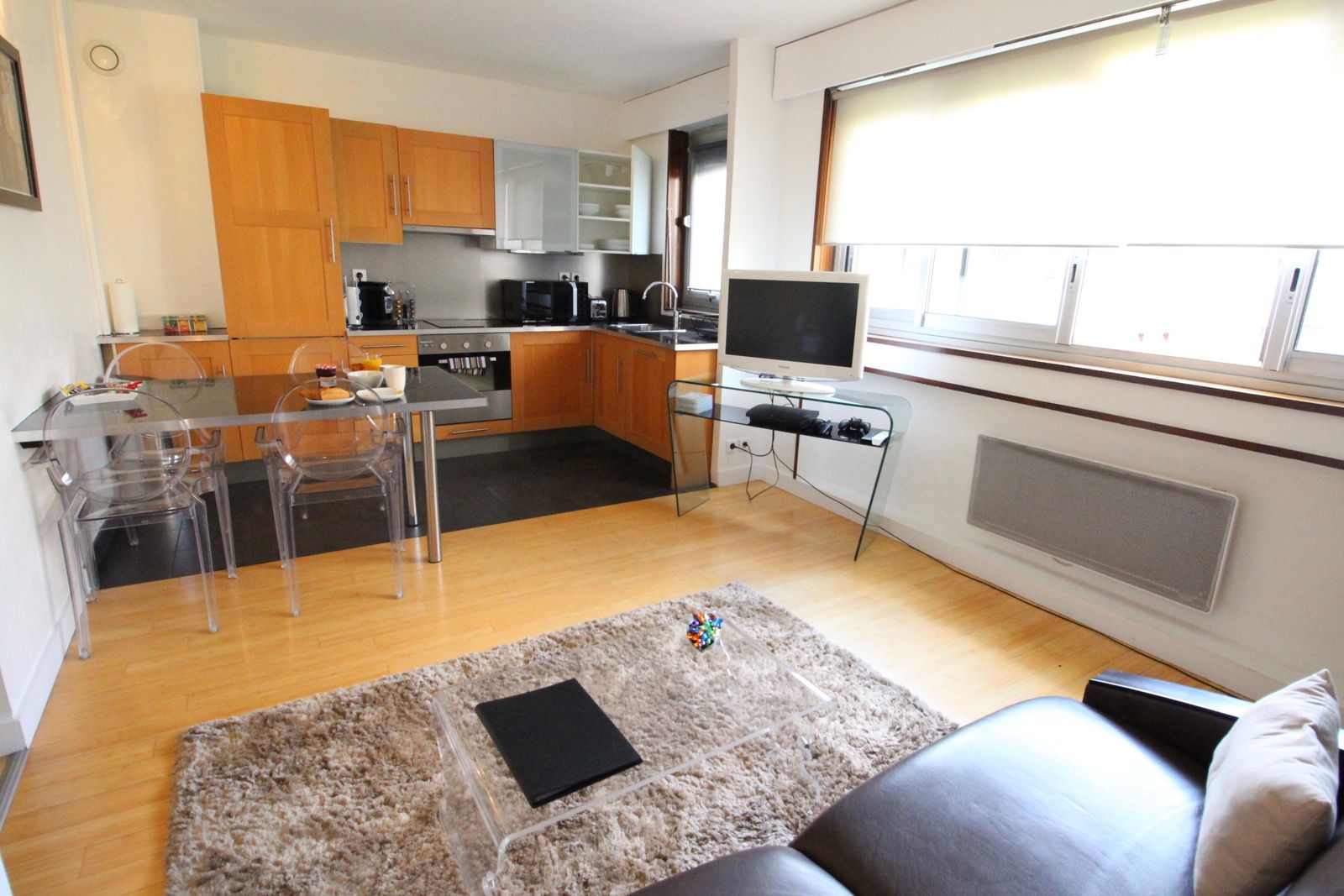 Spacious open-plan one-bedroom apartment with leather sofa, dining area, kitchen, and parquet floors at Short Stay Paris