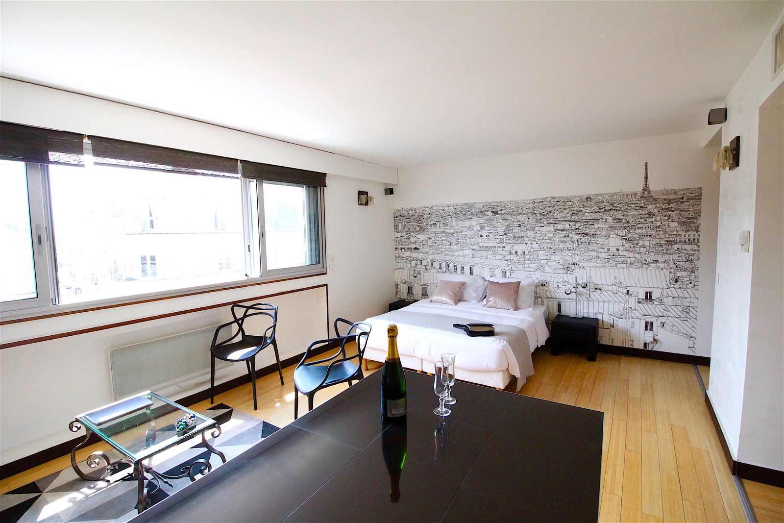 Elegant studio apartment with Paris skyline mural, kitchen bar with black stools, and parquet flooring at Short Stay Paris