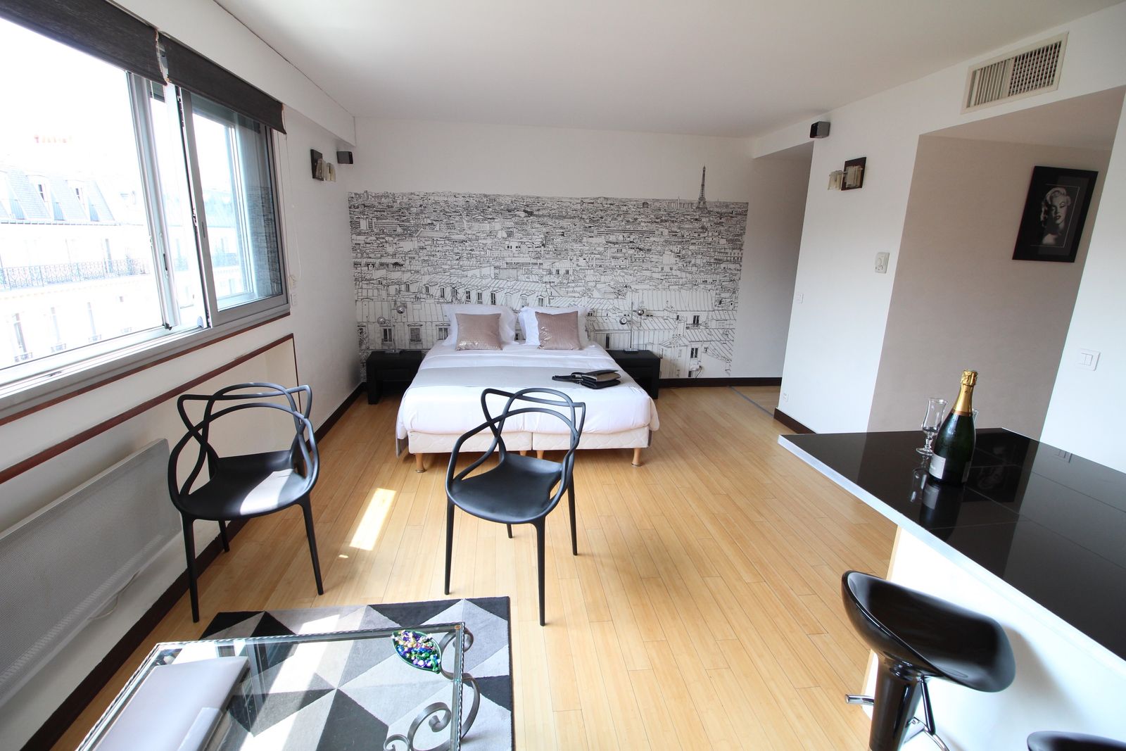 Studio apartment bed area with Eiffel Tower mural, seating nook, and welcome champagne service
